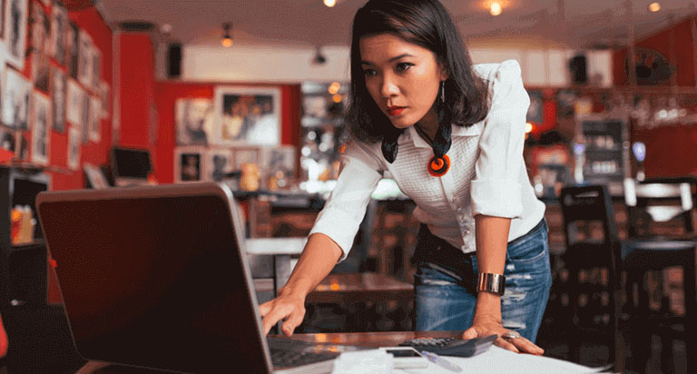 A woman focusing on her laptop screen and typing on her keyboard with her right hand