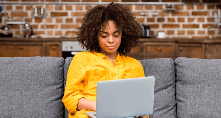 A woman sitting on a couch while looking at her laptop screen