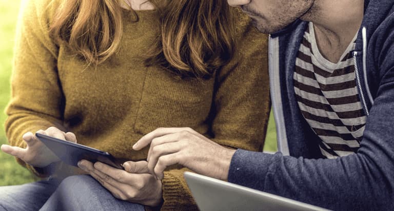 A woman holding a tablet sitting next to a man with a laptop sitting on his lap