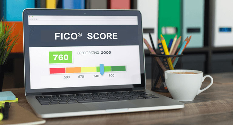 An opened laptop with a screen showing a FICO score of 760 which a sliding scale shows as GOOD with a white coffee mug and a cannister of pencils sitting next to the laptop