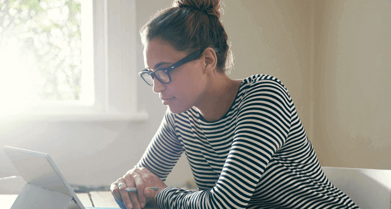 A woman wearing glasses looking at her tablet that is propped up on a stand