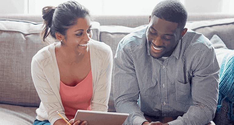 A woman and a man sitting next to each other smiling at a tablet