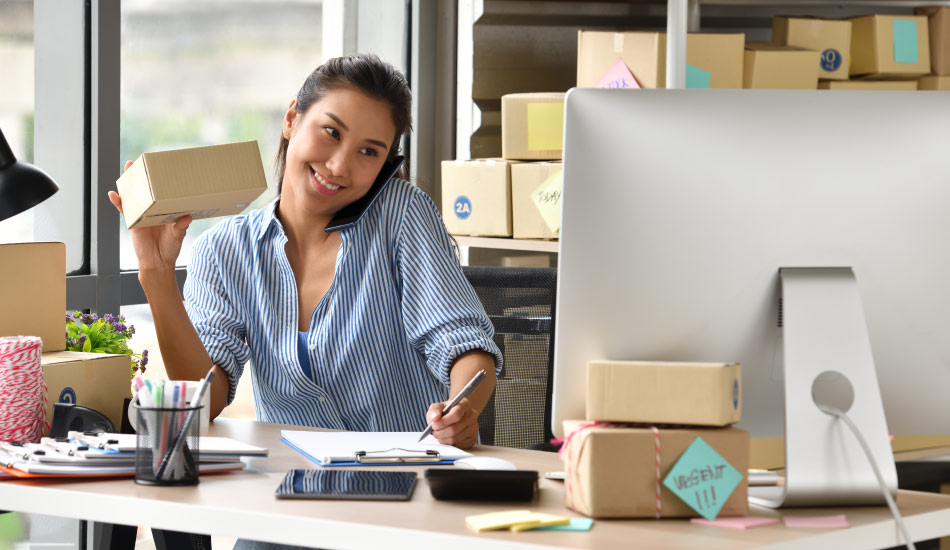 Mujer emprendedora revisa la logística de envios para cajas de cartón sobre su escritorio