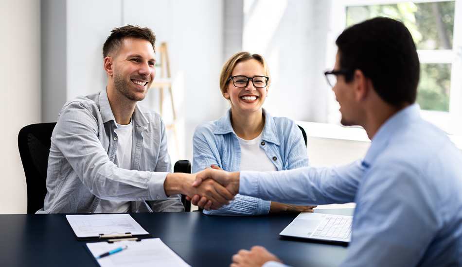 Pareja joven cierra un negocio con un vendedor mediante un apretón de manos y sonrisa en sus rostros