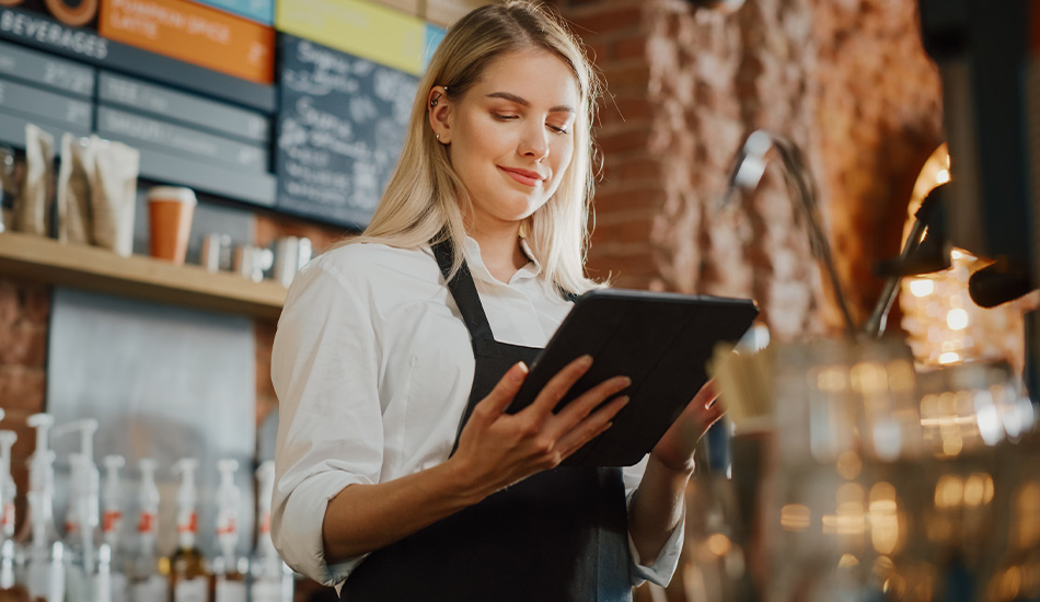 Mujer joven revisa los pedidos de la cafetería en la tableta que sostiene en su mano