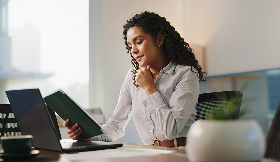 Mujer joven en su oficina compara datos entre su tableta y el computador