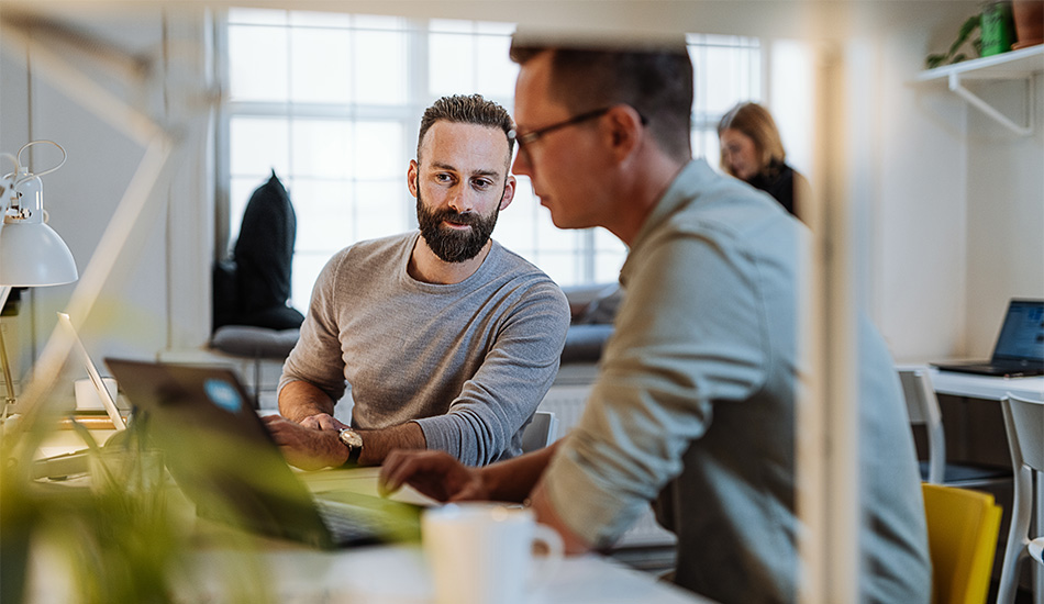 Dos hombres jóvenes revisan datos en una computadora mientras trabajan en la oficina