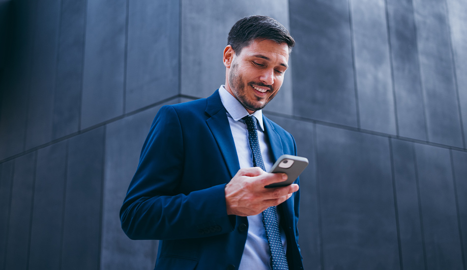 Joven ejecutivo revisa las notificaciones en su celular mientras camina en exteriores