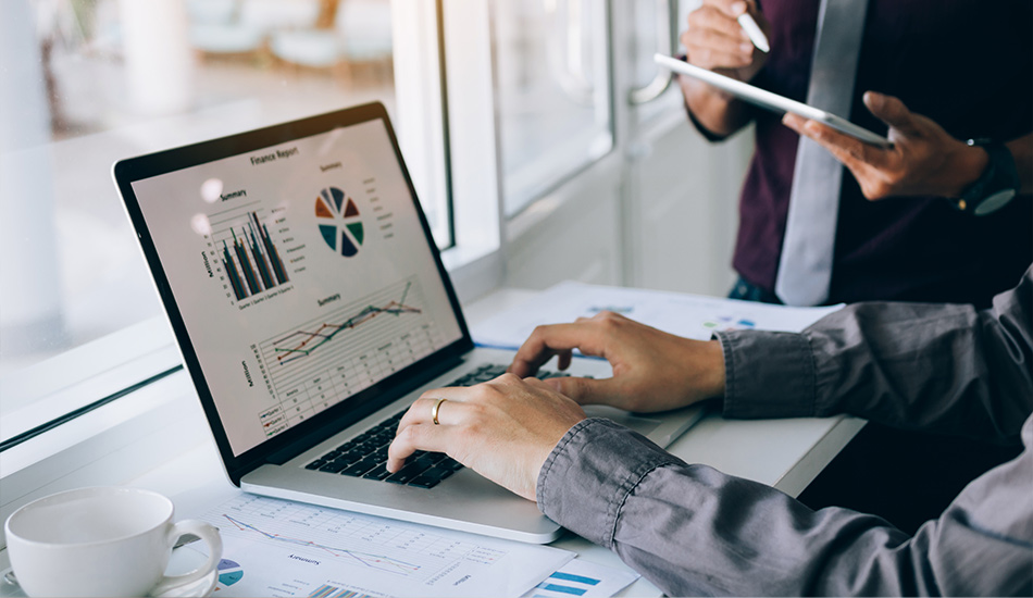 Joven termina un reporte de finanzas en su computador personal, en su escritorio junto a una taza de té