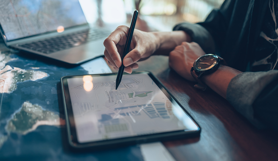 Joven navega un mapa interactivo en su tableta mientras muestra una dirección postar en su computador