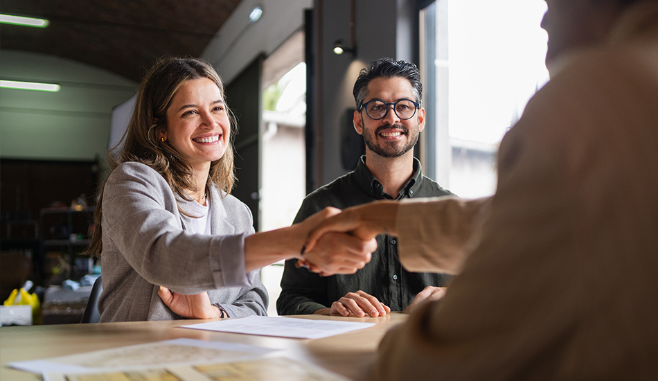 Pareja estrecha manos con vendedor tras firmar documento sobre la mesa