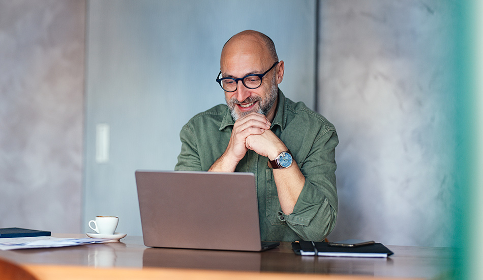 Señor calvo sonríe a su computador mientras ve algo en la pantalla