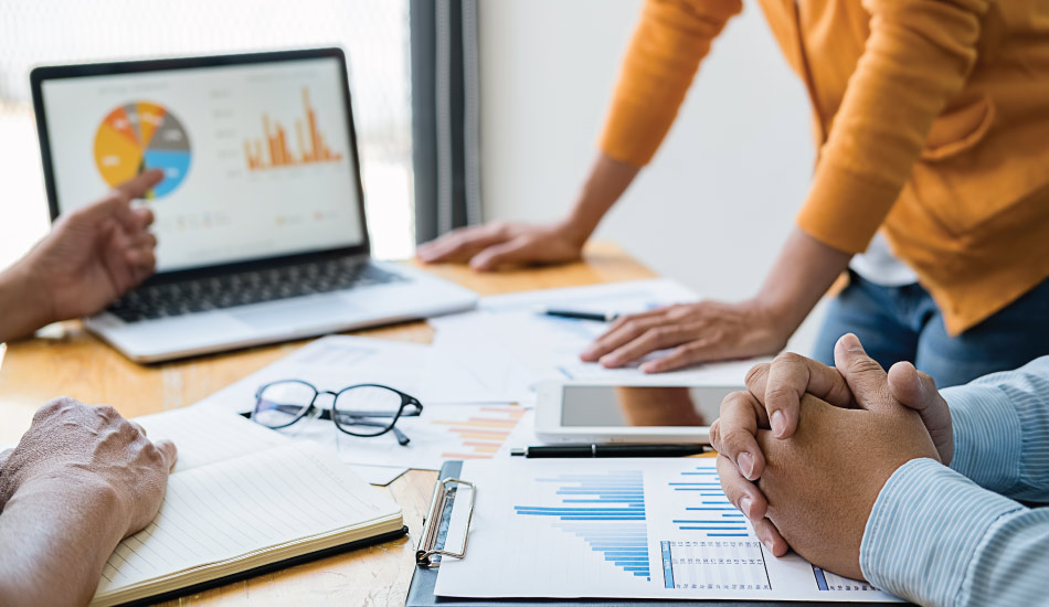 Office meeting around a large desktop with papers, documents and graphics on it