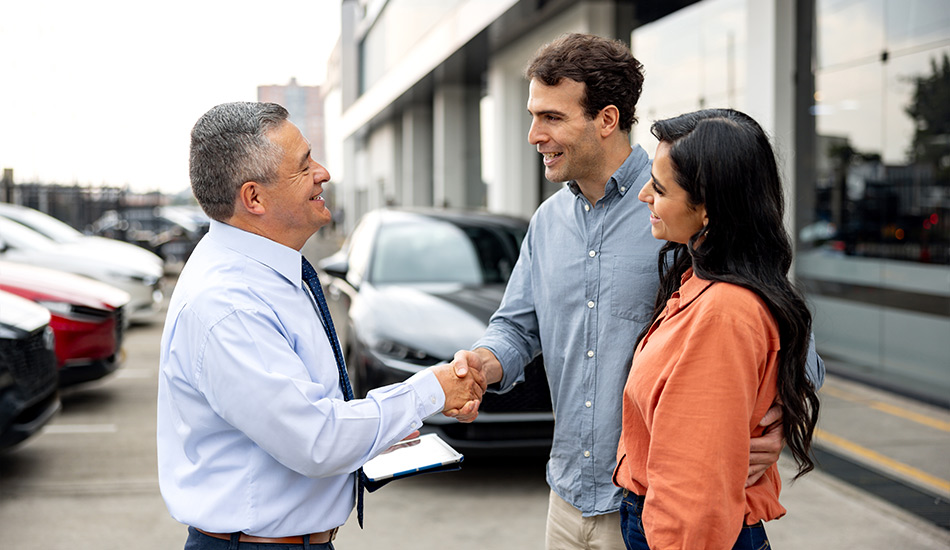 Pareja estrecha manos con un vendedor en la agencia de automóviles