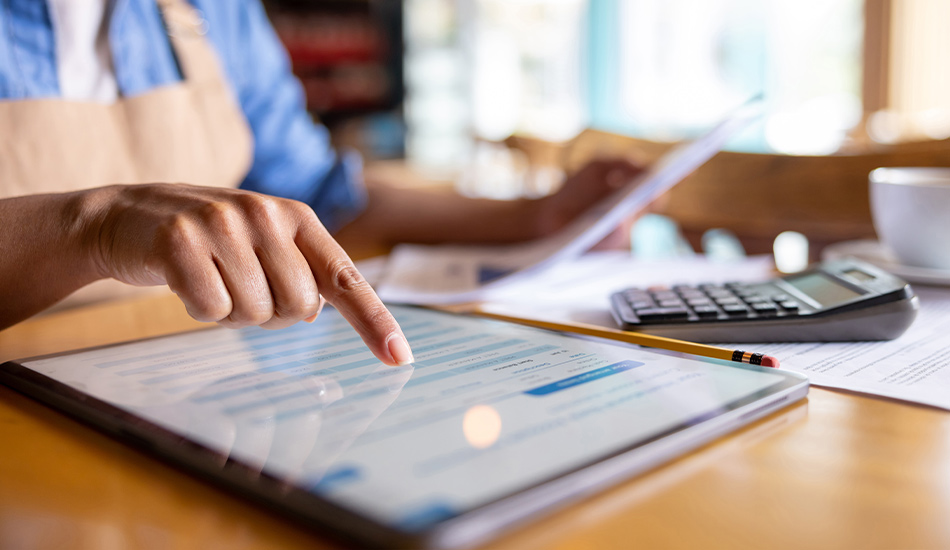 Mujer hace cálculos y sumas en su calculadora siguiendo una tabla de información en su tableta