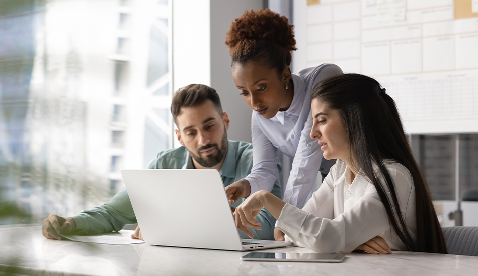 Tres personas jóvenes leen y señalan partes de un mismo documento sobre una computadora portátil