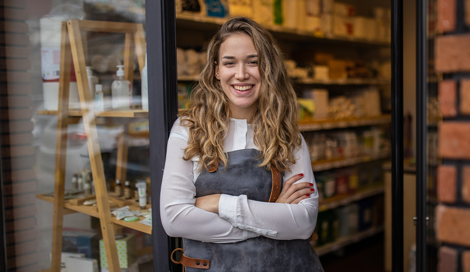 Joven emprendedora abre su tienda en la mañana y mira sonriente hacia afuera desde la puerta principal