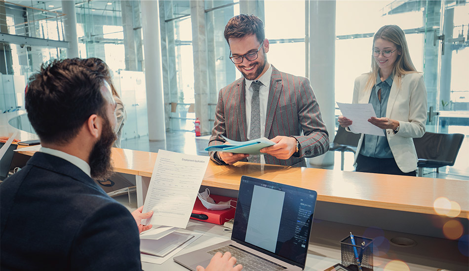 Joven sonriente en traje entero entrega una carpeta de papeles a un recepcionista
