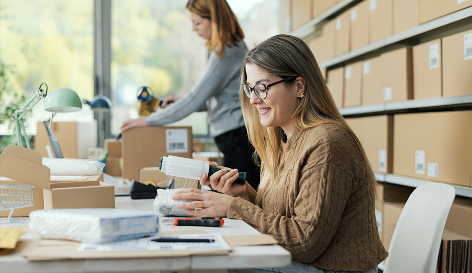 Mujer joven empaca felizmente una paquetería pequeña para su envío postal