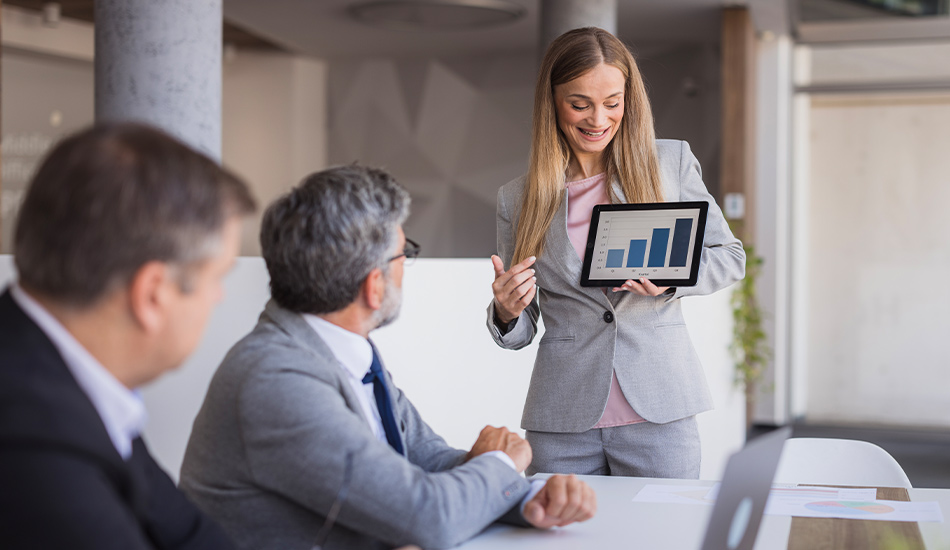 Mujer ejecutiva muestra un gráfico en su tableta frente a una sala de reuniones