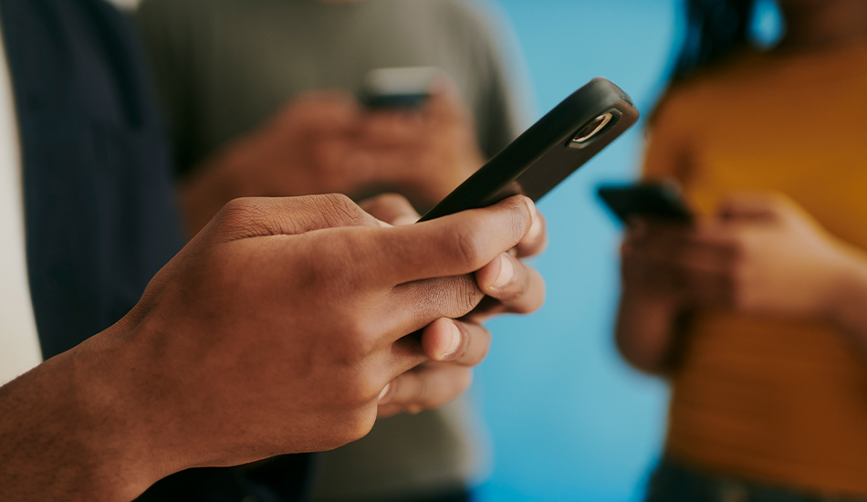 Manos de tres jóvenes teclean en sus dispositivos móviles