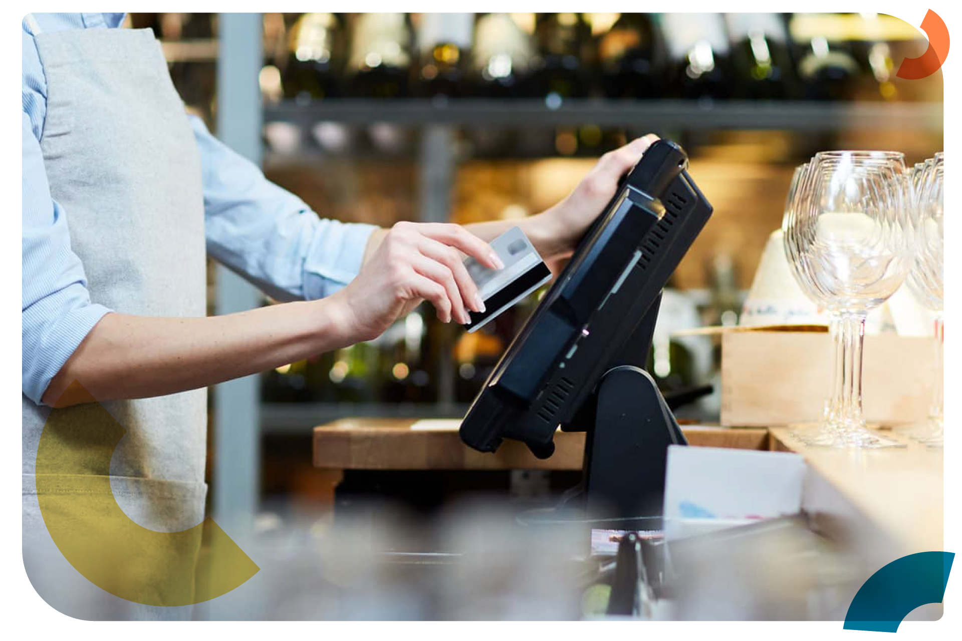 A narrow shot of a restaurant worker swiping a credit card with wine glasses in the background